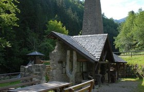 Historic smithy with fireplace in the forest, wooden tables in the foreground.