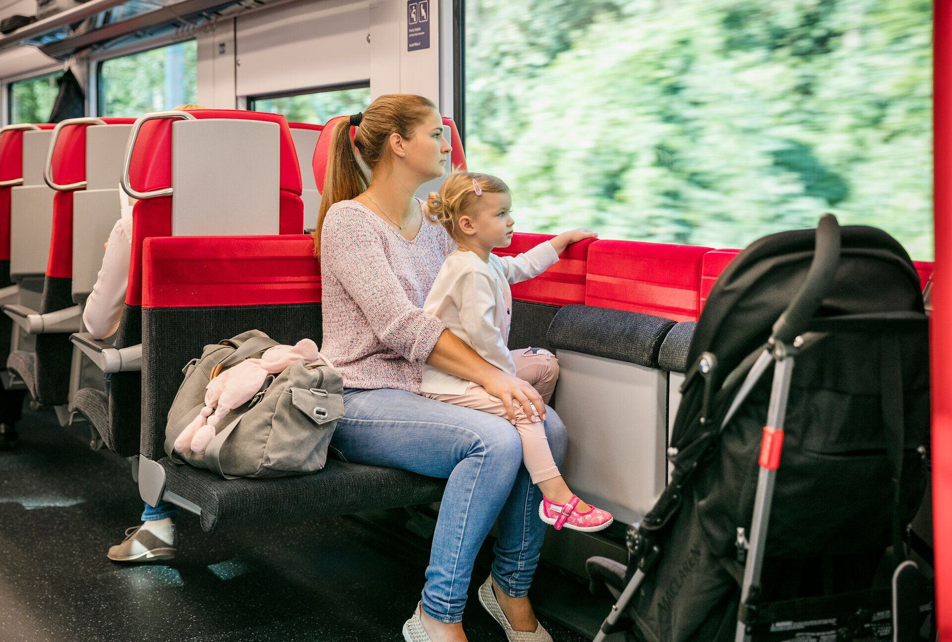 Eine Mutter und ihr kleines Kind genießen die entspannte Atmosphäre während ihrer Zugfahrt. Die vorbeiziehende Landschaft bietet einen malerischen Ausblick auf die Natur, während die beiden in Ruhe die Reise erleben.