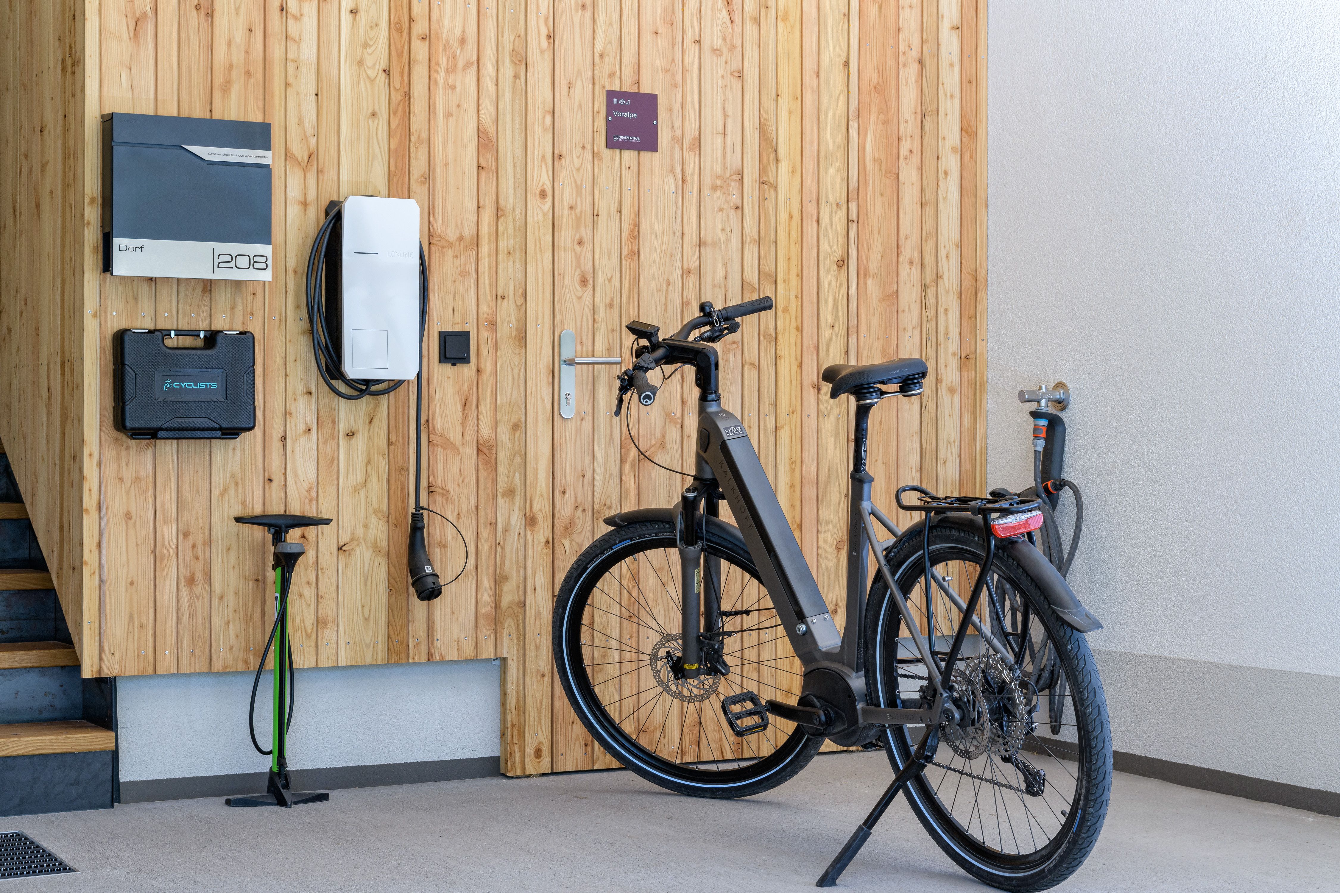A modern e-bike is parked in a garage next to a charging station mounted on a wooden wall.