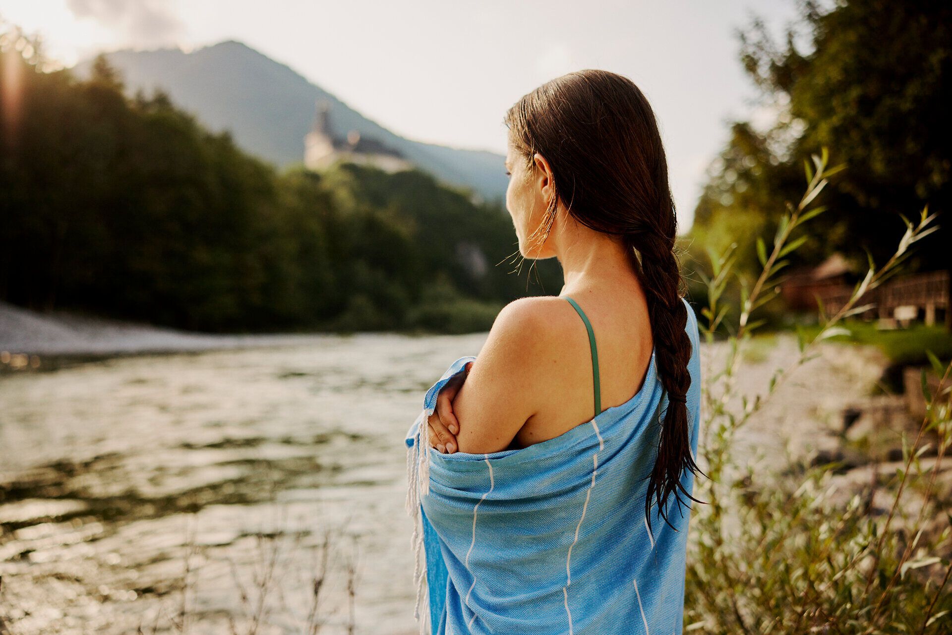 Ein sanfter Fluss schlängelt sich durch die malerische Landschaft, während die warmen Sonnenstrahlen auf das Wasser glitzern. Eine Frau genießt den Moment der Ruhe, umgeben von der üppigen Natur und den majestätischen Bergen des Mostviertels. Hier wird der Sommer in seiner schönsten Form erlebbar.