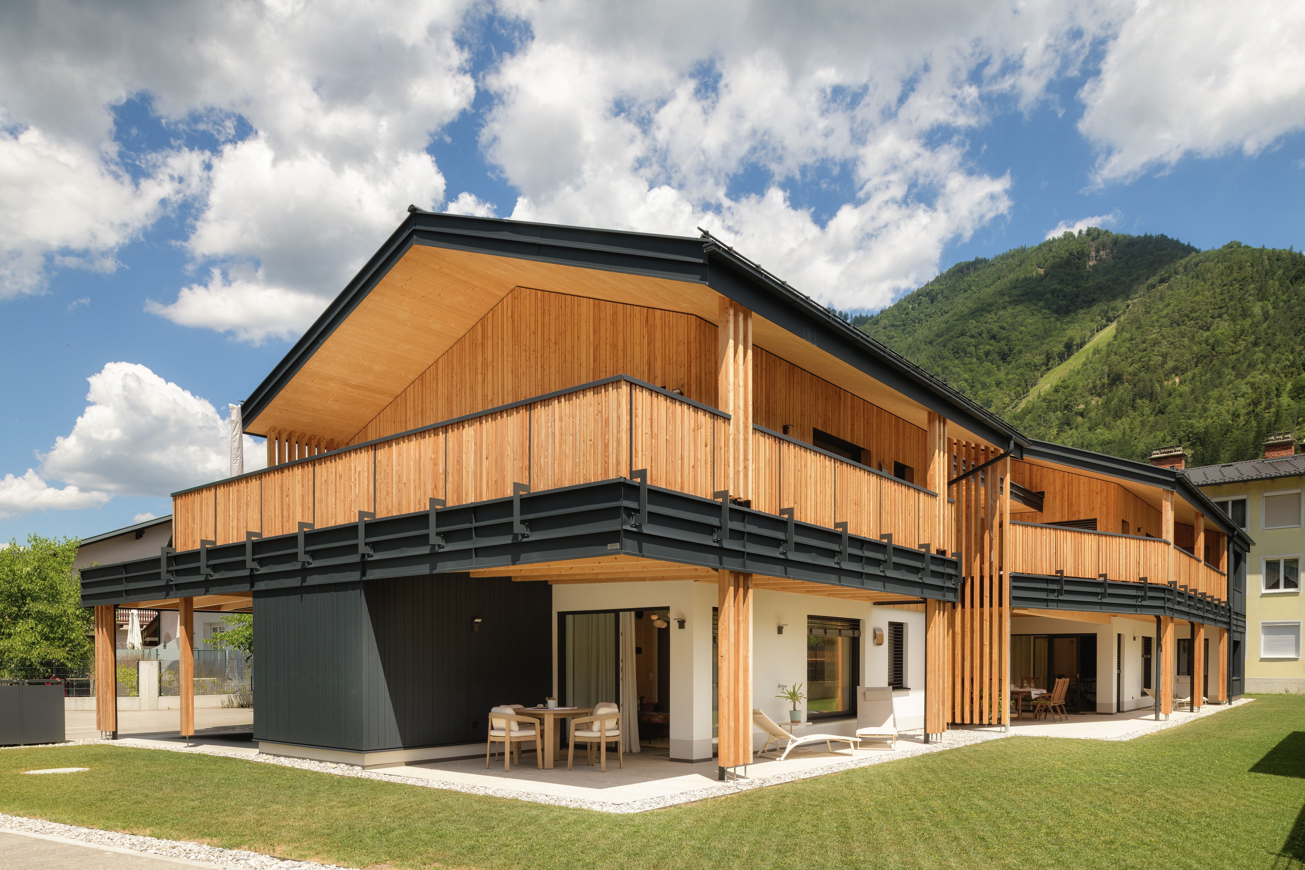 A modern wooden building with a balcony and a mountain backdrop.