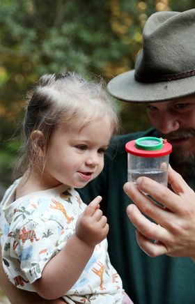 Mann zeigt einem Kleinkind eine Becherlupe in einem Wald im Naturpark NÖ Eisenwurzen. 