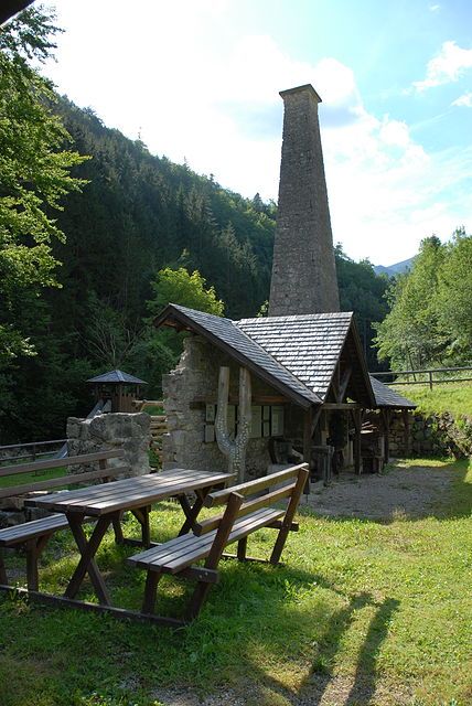 Historische Schmiede mit Kamin im Wald, Holztische im Vordergrund.