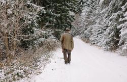Ein Jäger wandert durch eine verschneite Landschaft, umgeben von majestätischen Nadelbäumen. Die frische, kalte Luft und die Stille des Winters schaffen eine friedliche Atmosphäre, die zum Nachdenken und Entspannen einlädt.