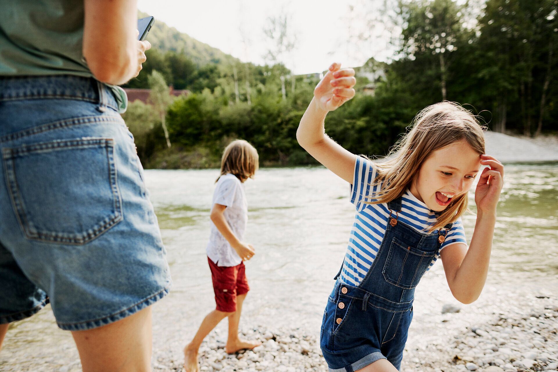 Ein fröhliches Familienabenteuer am Fluss, wo Kinder mit strahlenden Gesichtern im Wasser planschen. Die sanften Wellen und das glitzernde Licht schaffen eine unvergessliche Sommeratmosphäre, die zum Verweilen einlädt.