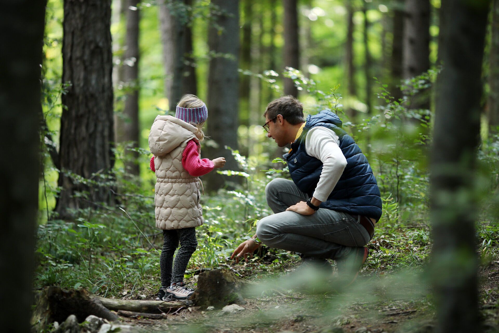 Ein Vater zeigt seinem Kind etwas Spannendes am Waldboden im Naturpark Hohe Wand. 