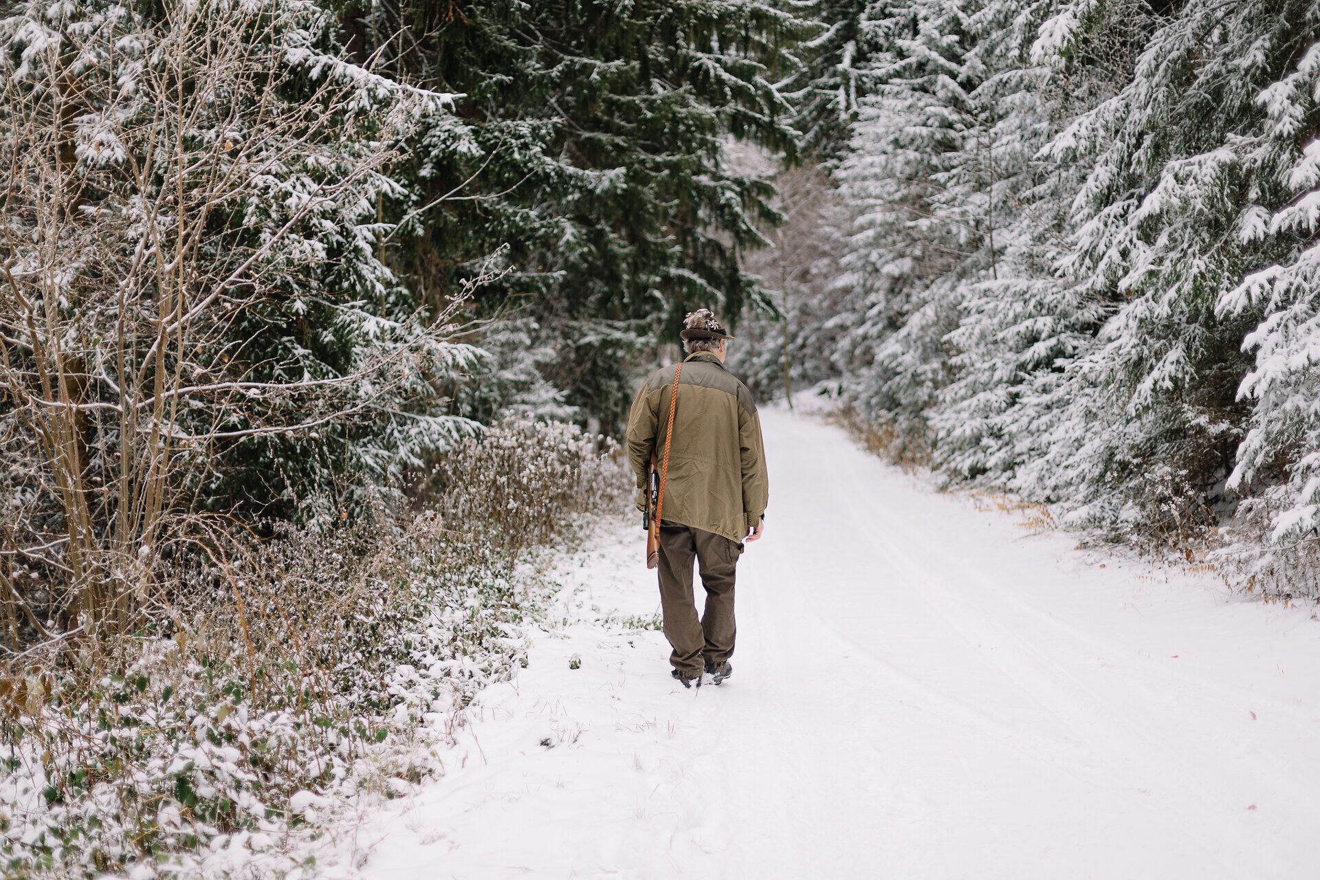 Ein Jäger wandert durch eine verschneite Landschaft, umgeben von majestätischen Nadelbäumen. Die frische, kalte Luft und die Stille des Winters schaffen eine friedliche Atmosphäre, die zum Nachdenken und Entspannen einlädt.