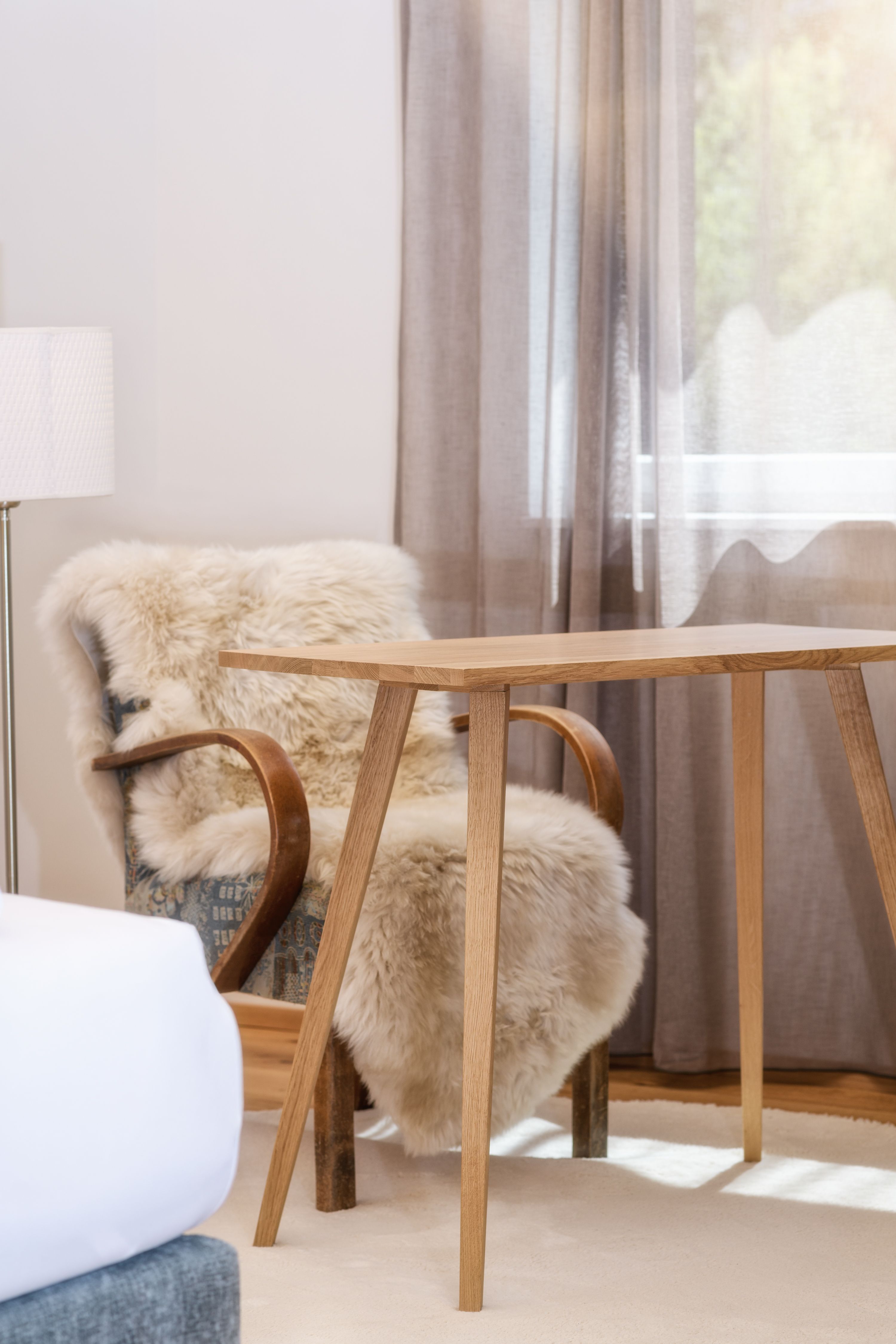 A cozy room with a wooden table, a chair with a fur throw, and a window with curtains.