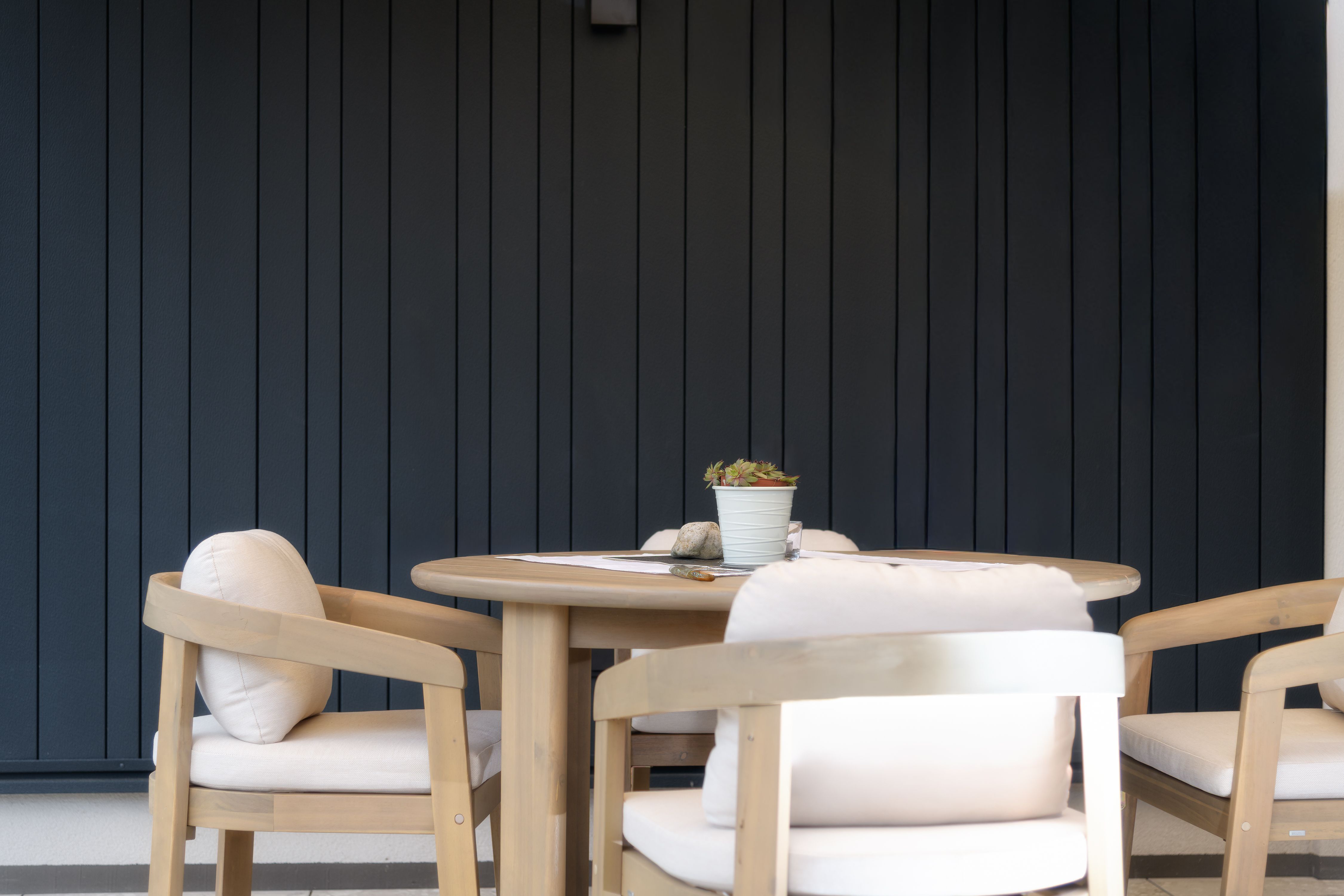A round wooden table with four upholstered chairs in front of a dark gray wall.