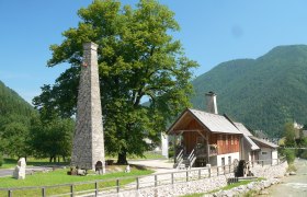 Historic building with chimney and water wheel in a rural setting.