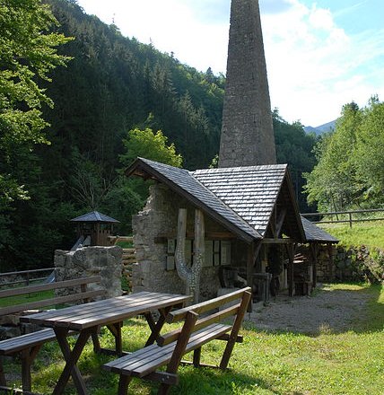 Historic smithy with fireplace in the forest, wooden tables in the foreground.