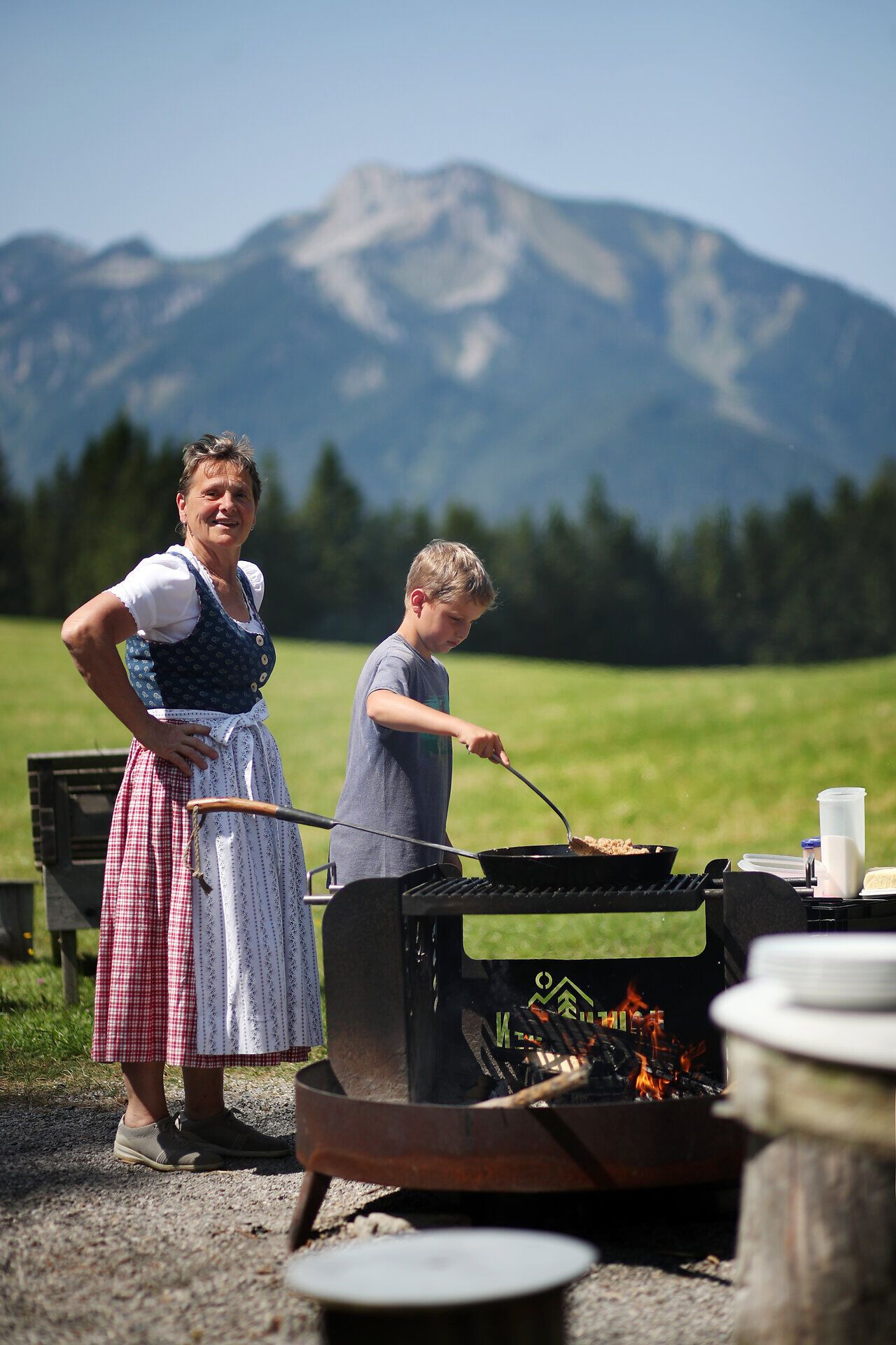 Eine Frau und ein Kind kochen mit einer großen Pfanne direkt am Feuer im Naturpark NÖ Eisenwurzen.