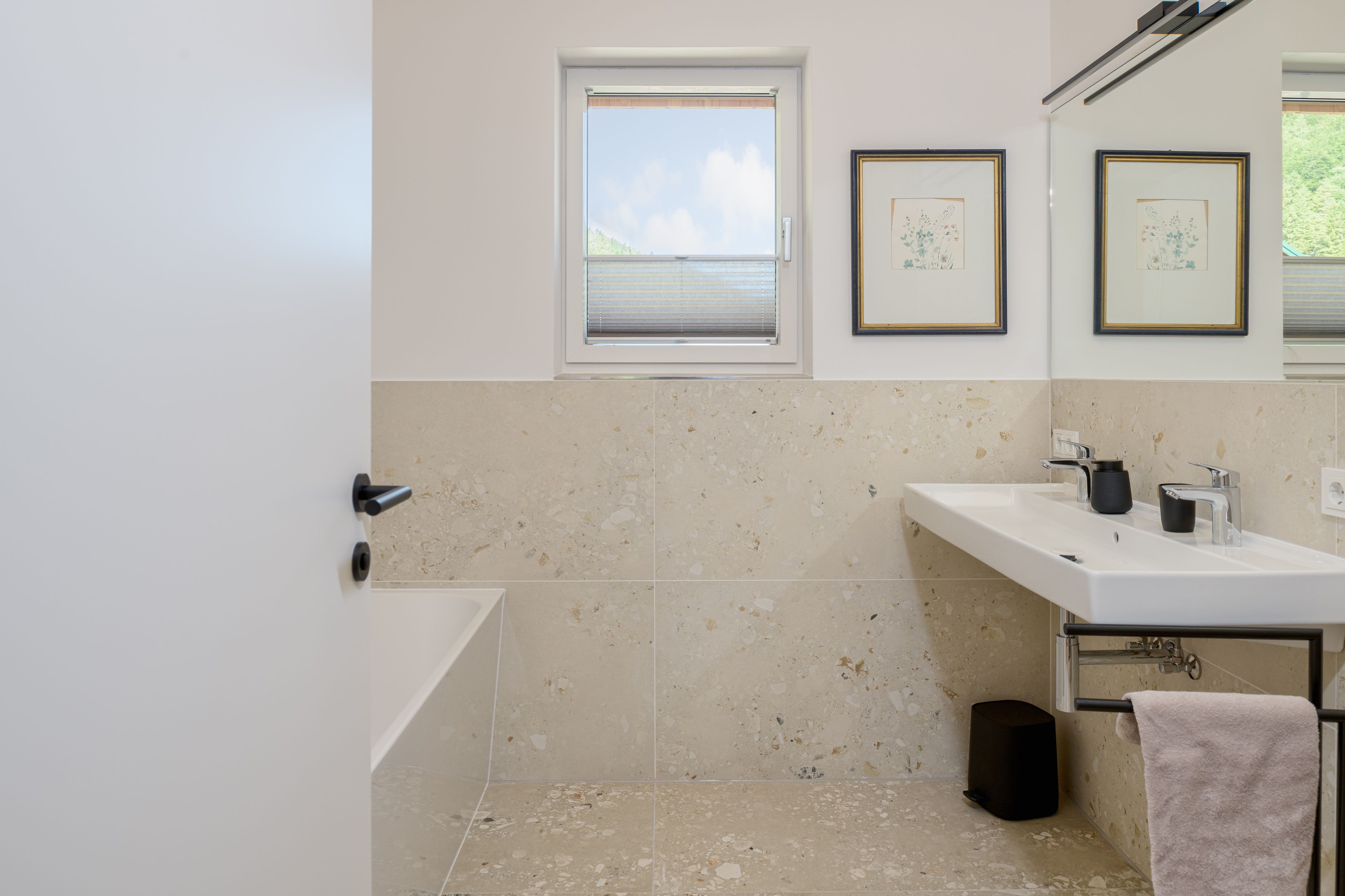 Modern bathroom with a window, double sinks, and a bathtub.